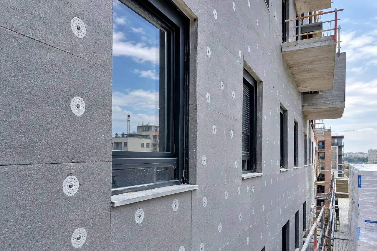 Fachada con el aislamiento térmico por el exterior a medio colocar, con andamio y balcones